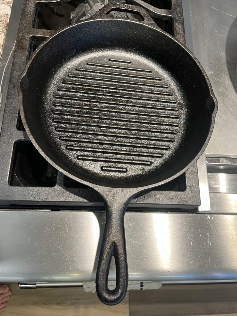 photo of a cast iron grill or grilling pan, sitting on a stainless steel stove or range