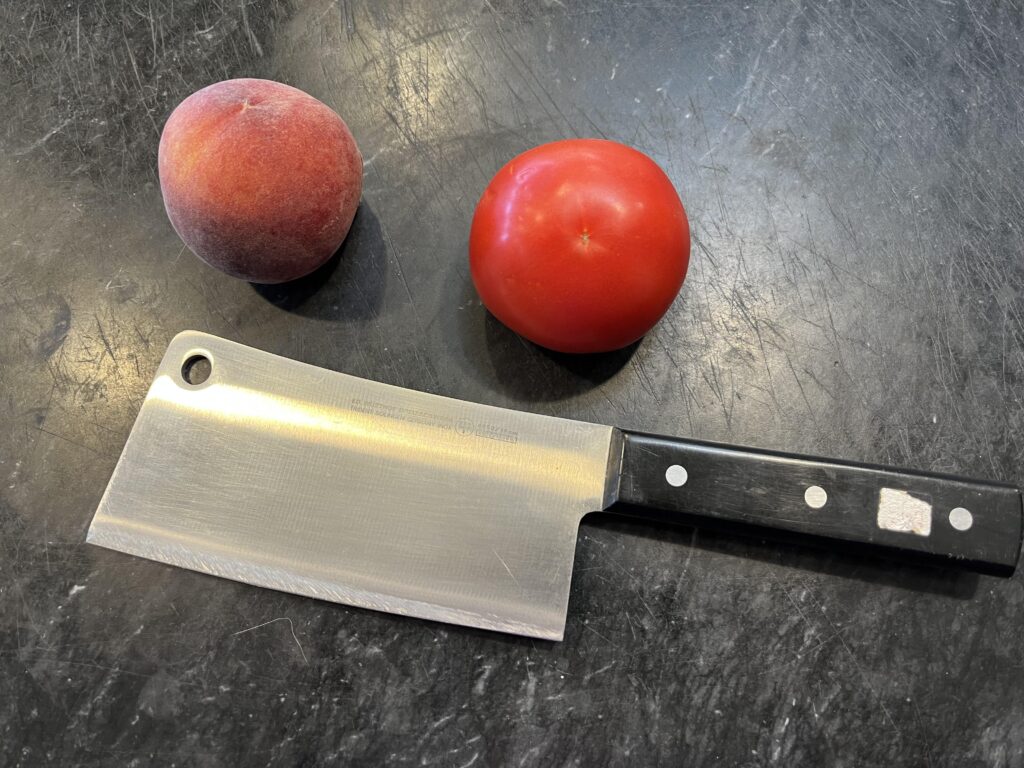 photo of a cleaver or meat cleaver knife on a black marble board with two tomatoes to show scale