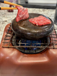 a photo of a piece of raw Wagyu beef being placed on a hot stone grill