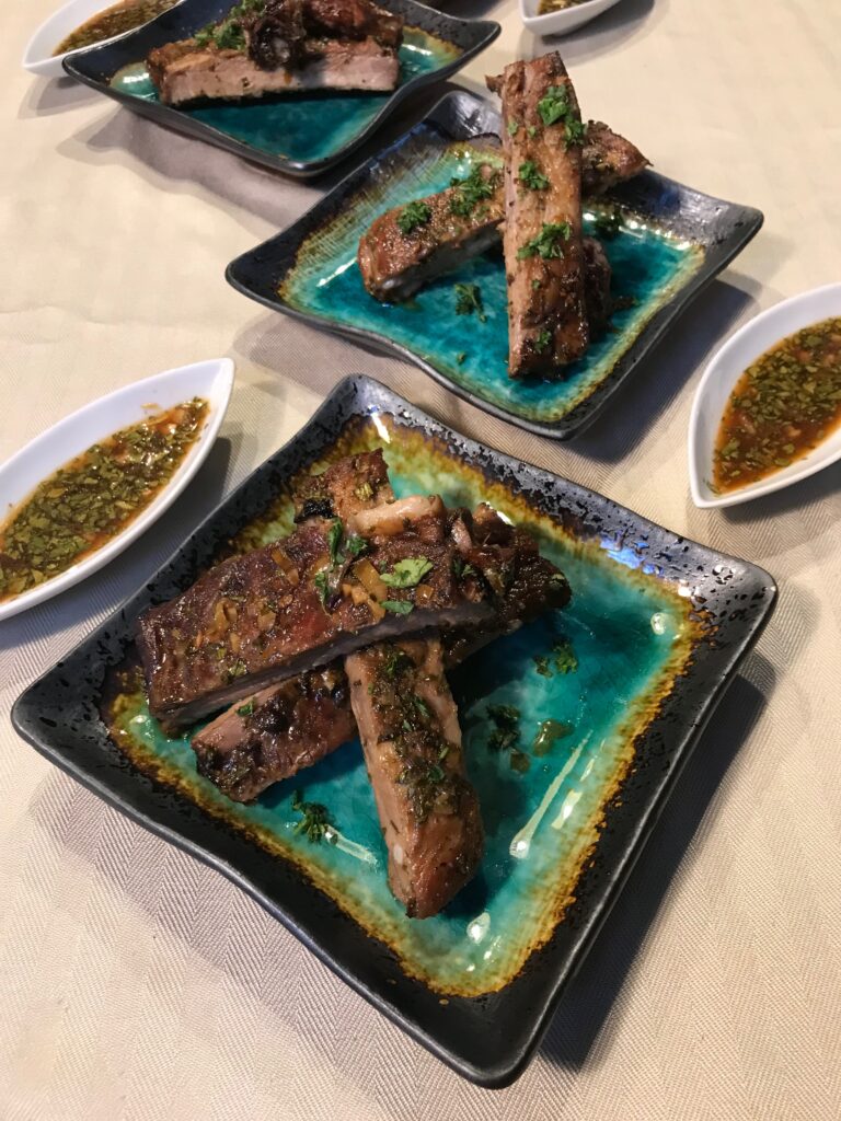 A plate of smoked and seared St. Louis style pork spare ribs on a Japanese green plate with citrus dipping sauce in a white almond-shaped plate