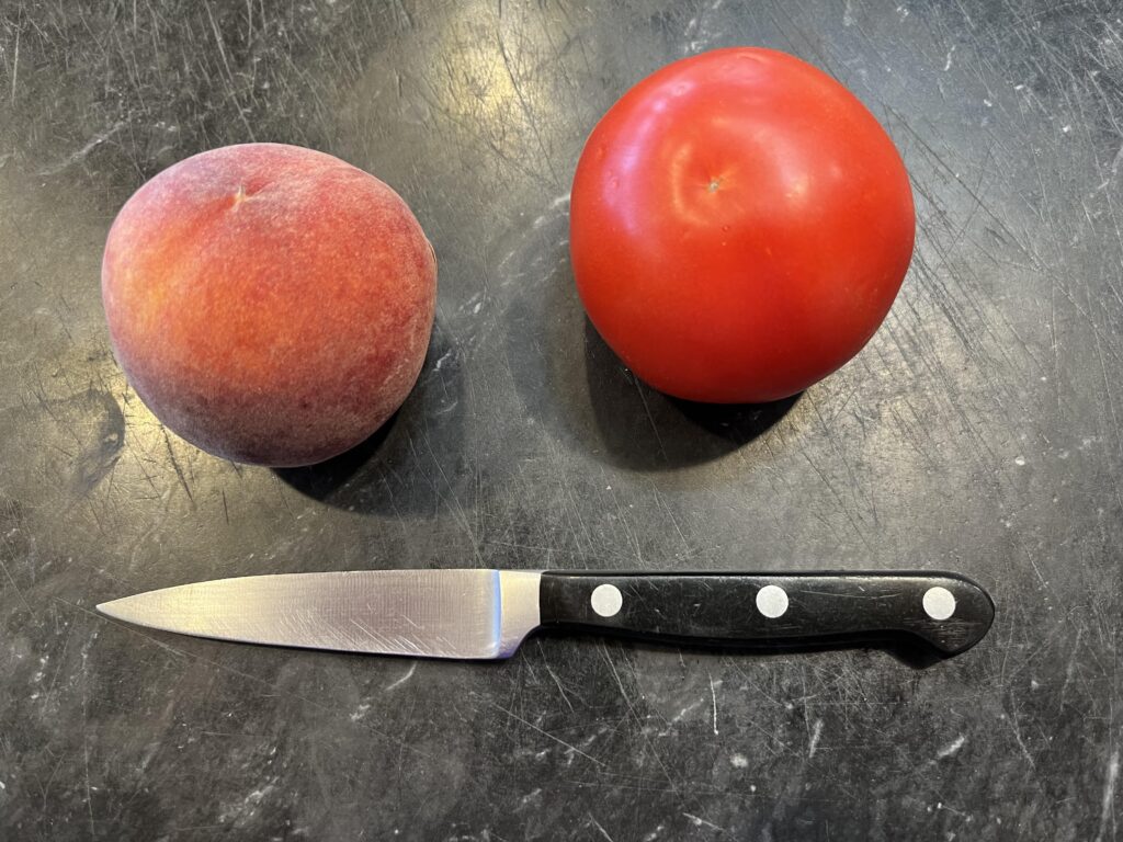 photo of a paring knife on a black marble board with two tomatoes to show scale