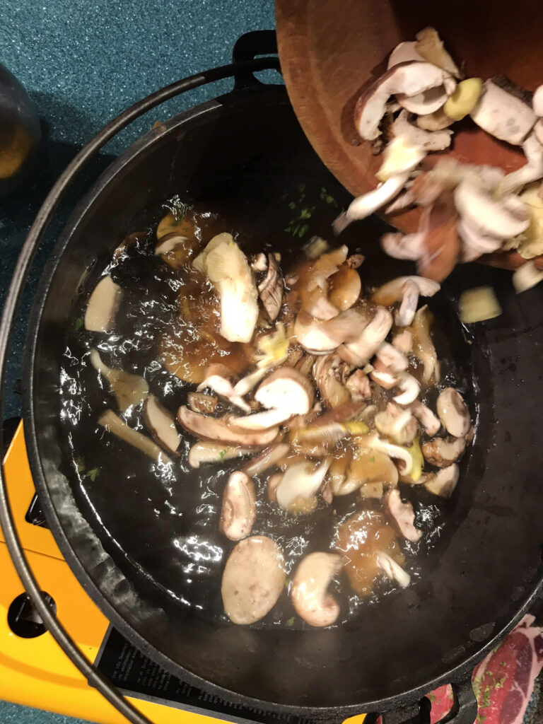 mushrooms beings poured or added to a Dutch oven cast iron pot on a butane stove or burner; this photo illustrates the text