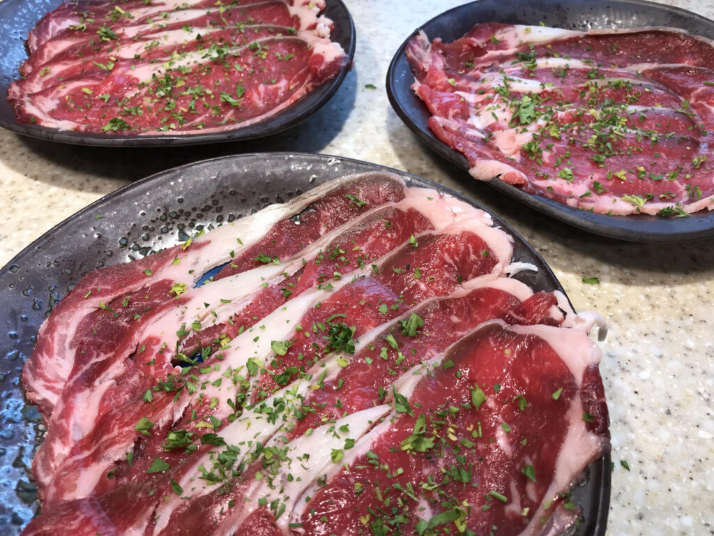 a plate of thinly sliced marbled beef sprinkled with parsley for beef shabu shabu Japanese hotpot; this photo illustrates the text