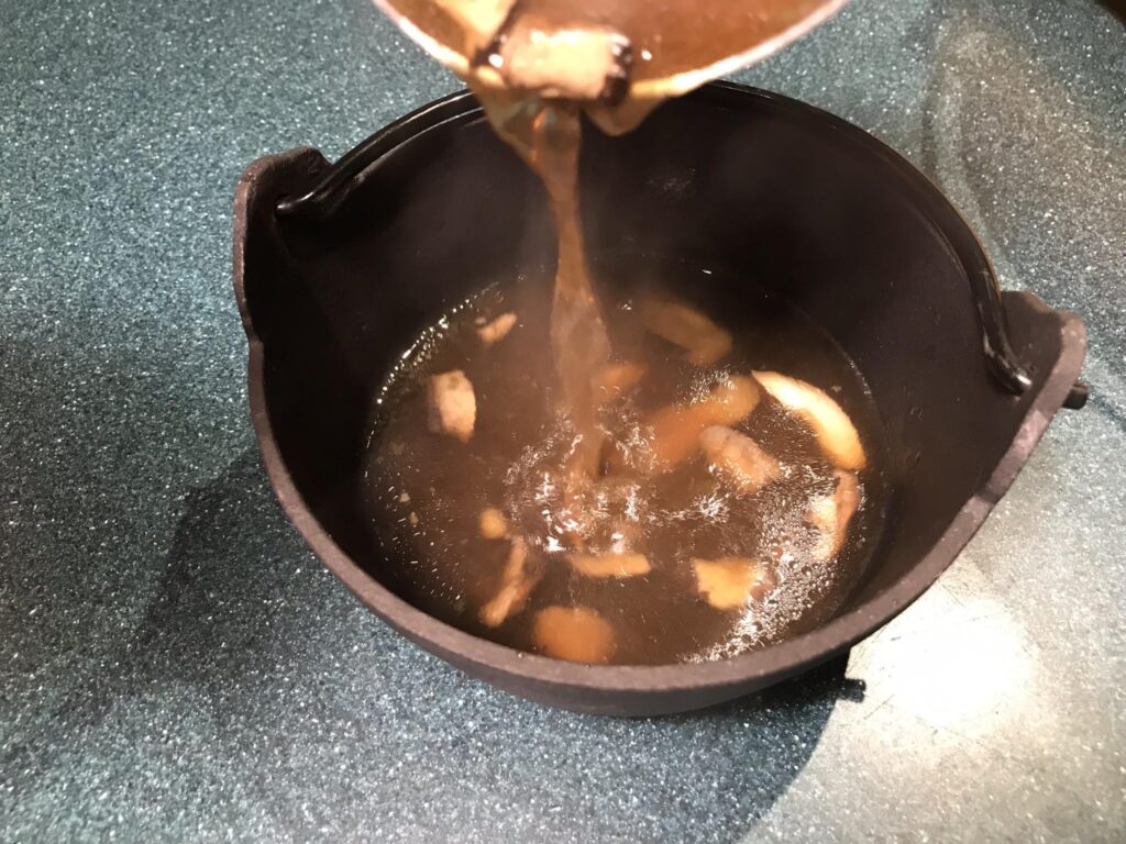 Japanese beef shabu shabu broth with mushrooms being poured into an iron bowl; this photo illustrates the text