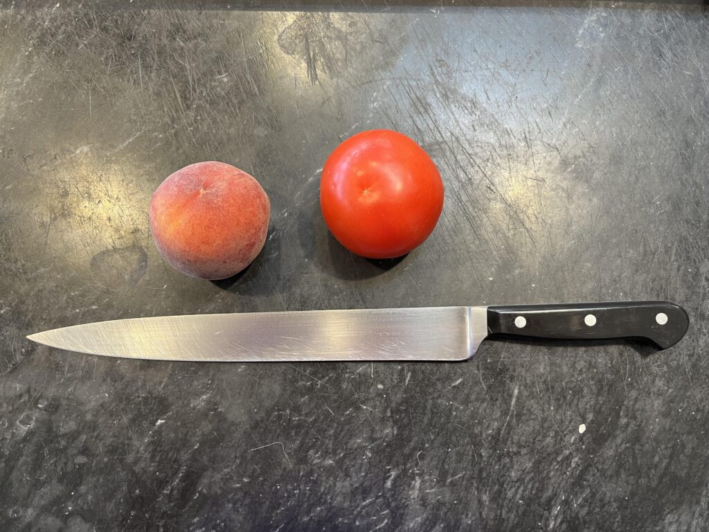 photo of a slicer or slicing knife on a black marble board with two tomatoes to show scale