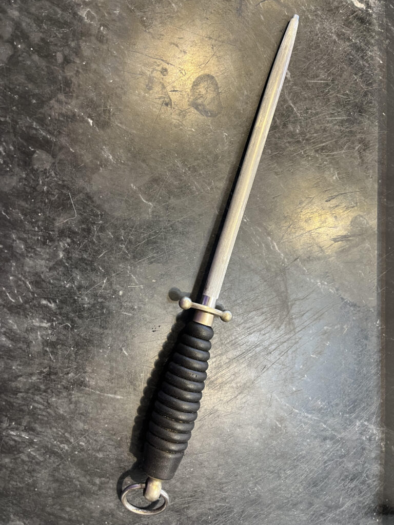 photo of a sharpening or honing steel for kitchen knives on a black marble board with two tomatoes to show scale