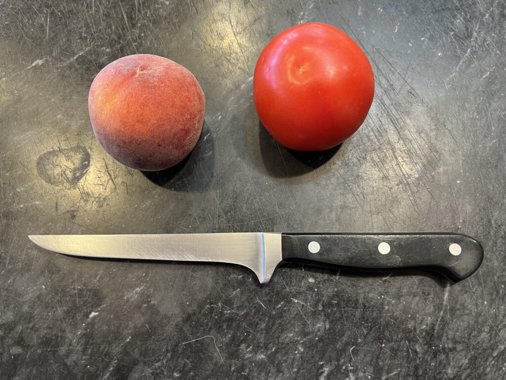Wusthof brand boning knife on a black marble board with a tomato and a peach