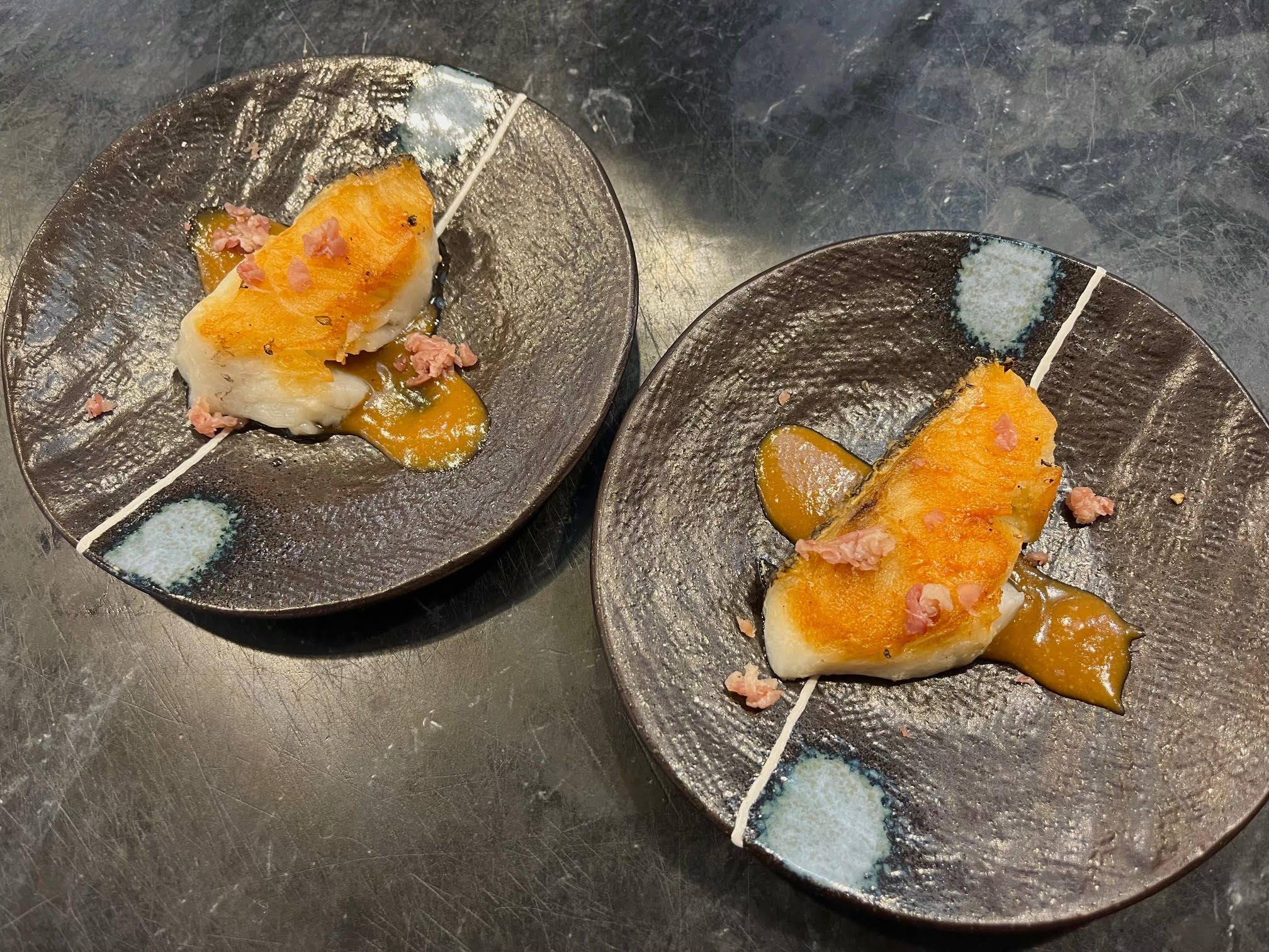 two plates, each with a piece of seared Chilean Sea Bass over a streak of miso sauce