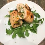 Two diagonally sliced halves of a chicken roulade rollup on a bed of arugula on a white plate