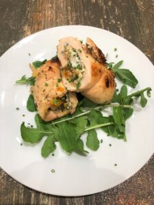 Two diagonally sliced halves of a chicken roulade rollup on a bed of arugula on a white plate