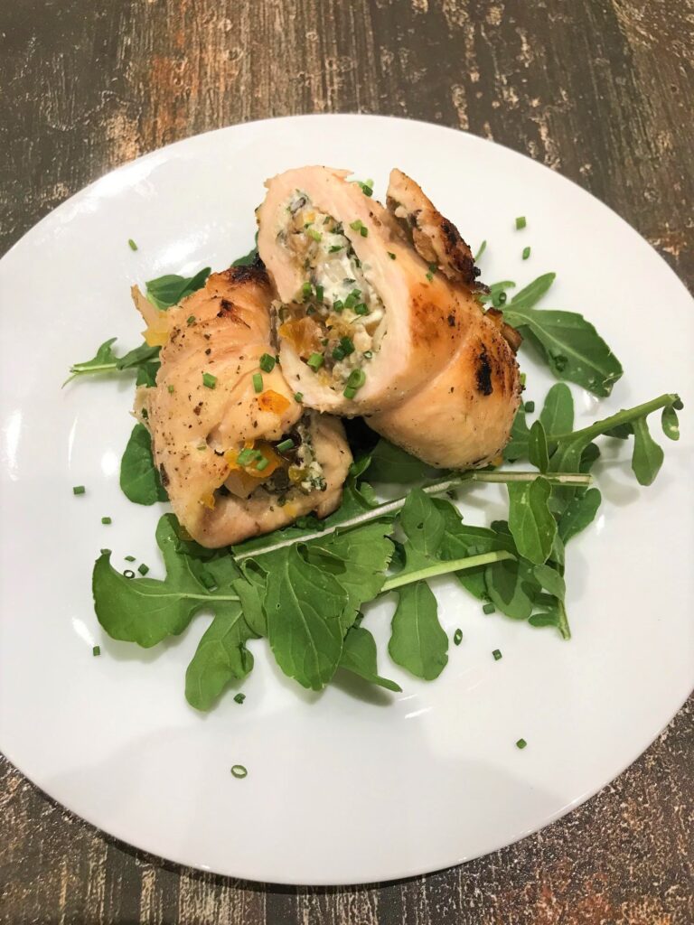 Two diagonally sliced halves of a chicken roulade rollup on a bed of arugula on a white plate