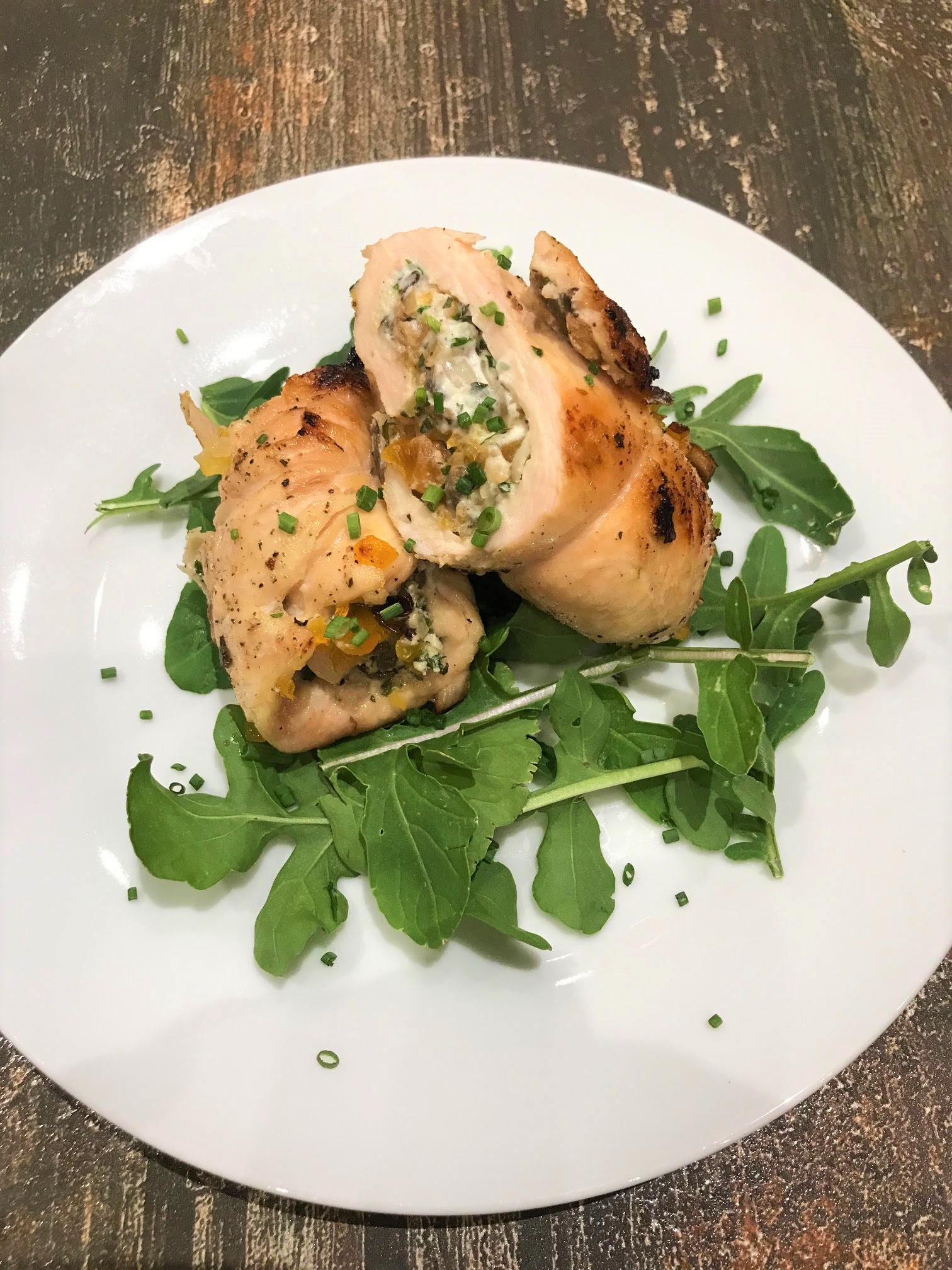 Two diagonally sliced halves of a chicken roulade rollup on a bed of arugula on a white plate
