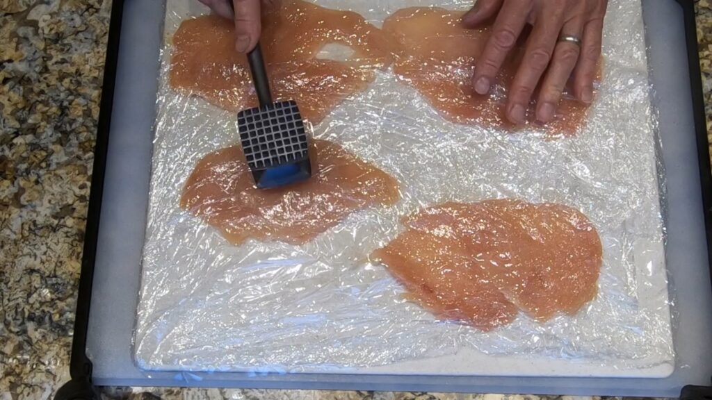 pounding out chicken breasts covered with plastic wrap