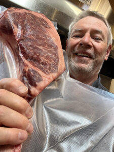 photo of the smiling author holding a vacuum sealed tomahawk steak