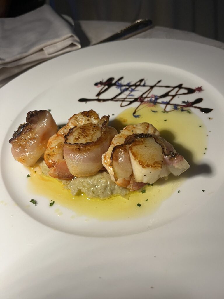 Capasante Lardo scallops wrapped in bacon on a white plate