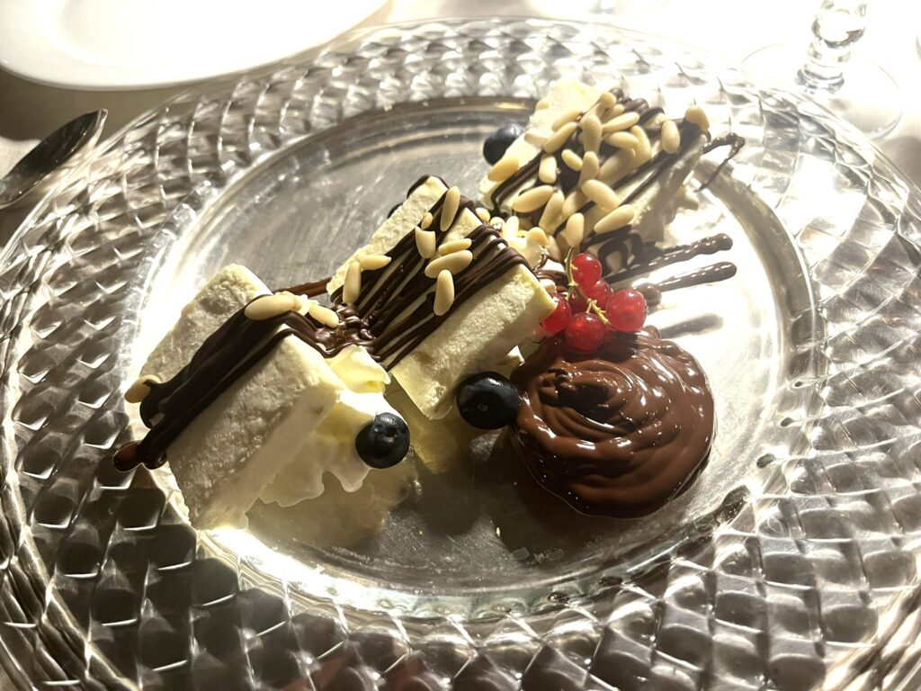 dessert of sweat baked bar, two types of chocolate, red currants, blueberries, and pine nuts on a glass plate