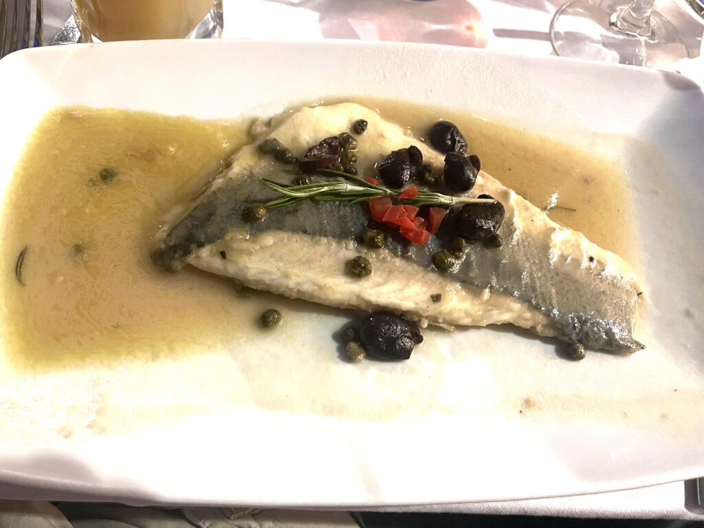 Pesce alla Vernaccia fish with capers and olives on a white plate