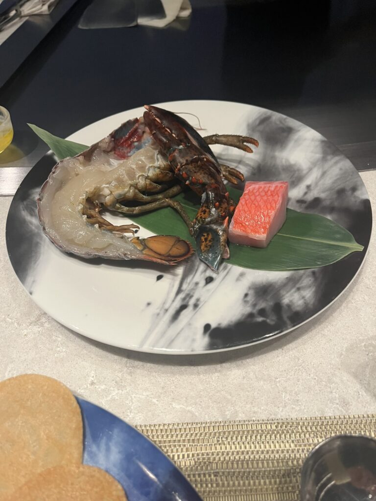 uncooked half lobtser and a piece of uncooked red snapper fish on a green leaf on a plate