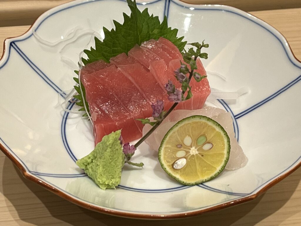 tuna sashimi slices on a plate with a small mound of freshly grated wasabi, a slice of yuzu citrus fruit, and some white fish sashimi