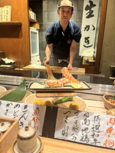 photo of food fresh food choices, a robata chef handing a guest food on a long paddle, and the interior of Inakaya Ginza in Tokyo Japan
