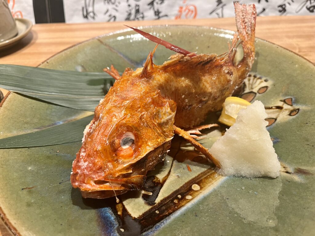 a grilled red fish with a mound of grated daikon on a green place with two green leaves