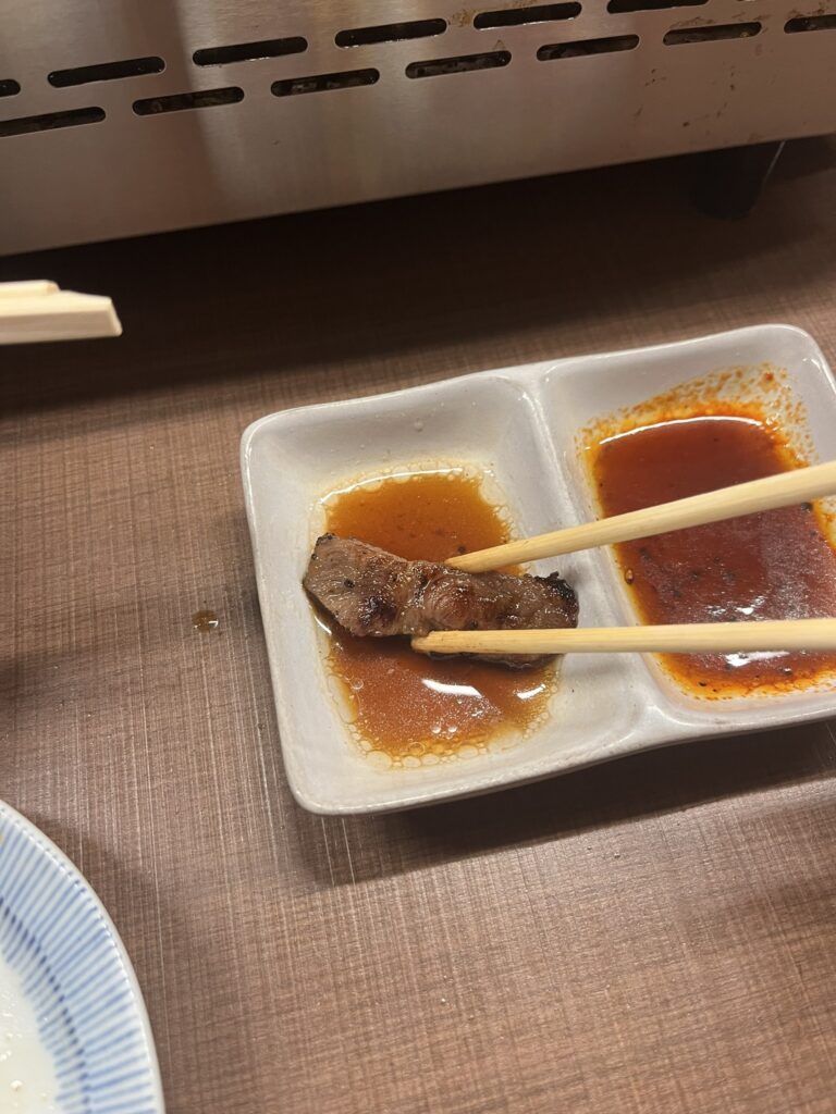 chopsticks dipping a piece of cooked beef into sauce 