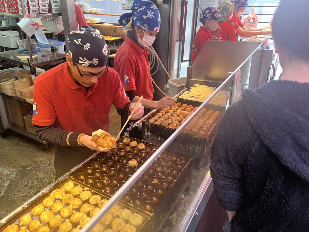 cooks grilling Takoyaki at a street stand in Osaka Japan