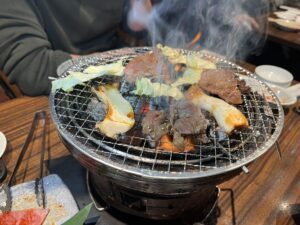 beef and vegetables being cooked on a yakiniku charcoal grill
