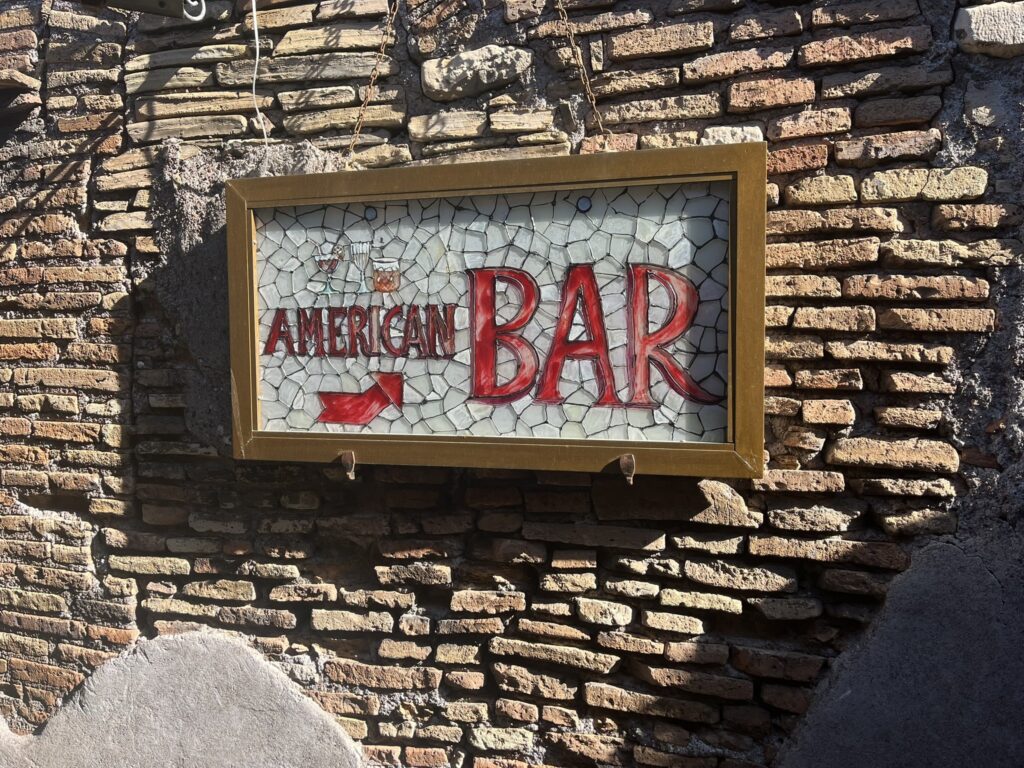brick wall with a sign pointing to the American Bar in the Hotel Forum in Rome Italy