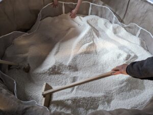 sake brewery worker raking rice in a sake steamer