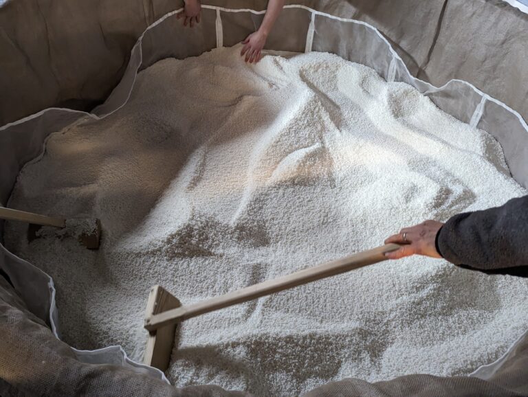 sake brewery worker raking rice in a sake steamer