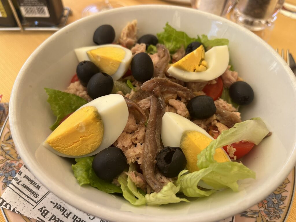 Italian version of Salad Nicoise with hard-boiled egg, lettuce, anchovies, tuna, and olives in a white bowl