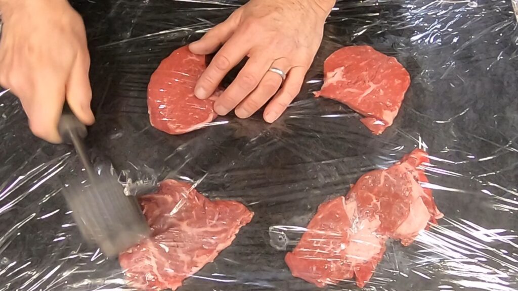 pounding beef medallions on a black board with a meat pounder