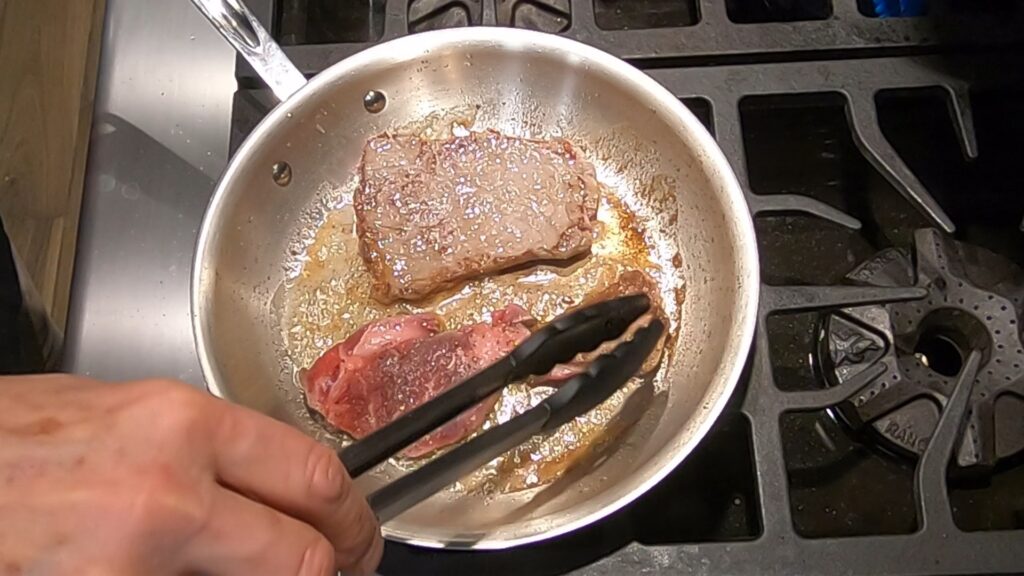 browned and partially cooked beef medallions being flipped in a saute pan