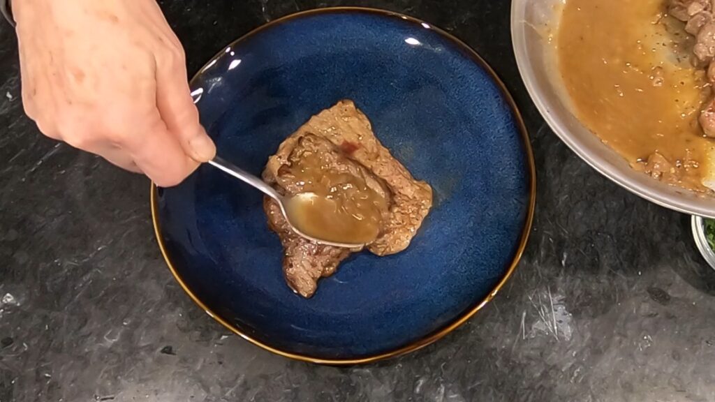 spooning sauce over a beef medallion on a blue plate